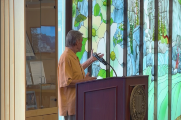 Bill Poulson speaks at podium in front of bookcase and spring Yosemite mural