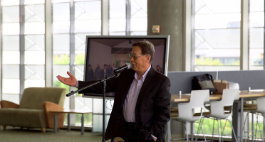 Haipeng Li stands and speaks at microphone and gestures to the crowd with an outstretched hand