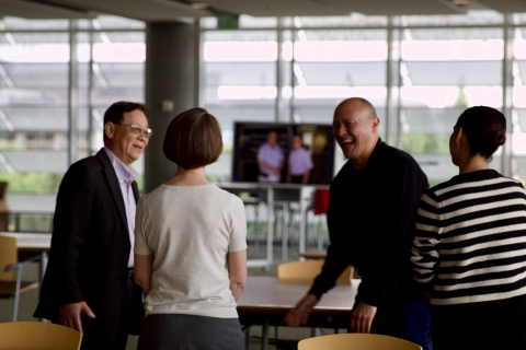 Four individuals stand in a semi-circle, visiting and laughing