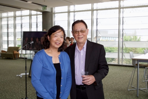 Xiaoping and Haipeng Li stand and smile; microphone and slideshow display in background