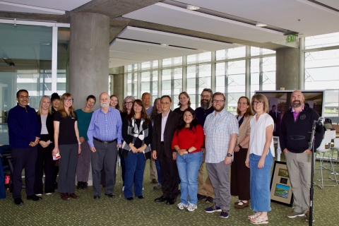 A group of almost 20 individuals stand in a semi-circle and smile