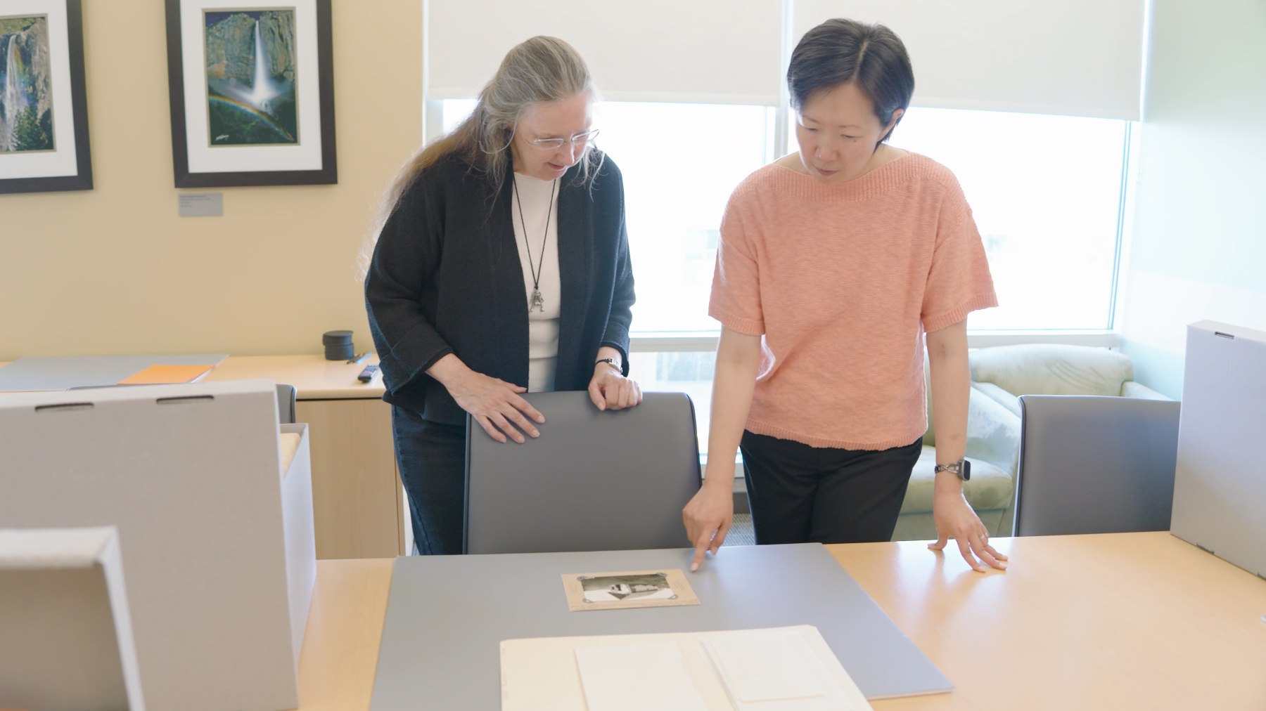 Two individuals behind table, looking down at archival materials