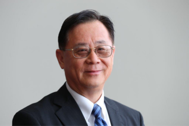 Headshot of Haipeng Li wearing a dark gray suite, white dress shirt, blue tie, he is wearing glasses