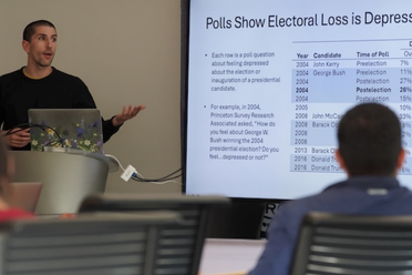 Political science professor Ojeda presents. Screen at right. Student in audience listen.